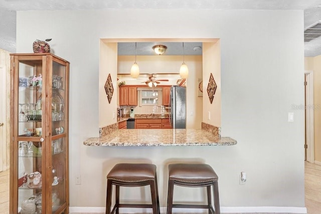 kitchen with kitchen peninsula, hanging light fixtures, light stone counters, a breakfast bar area, and stainless steel appliances