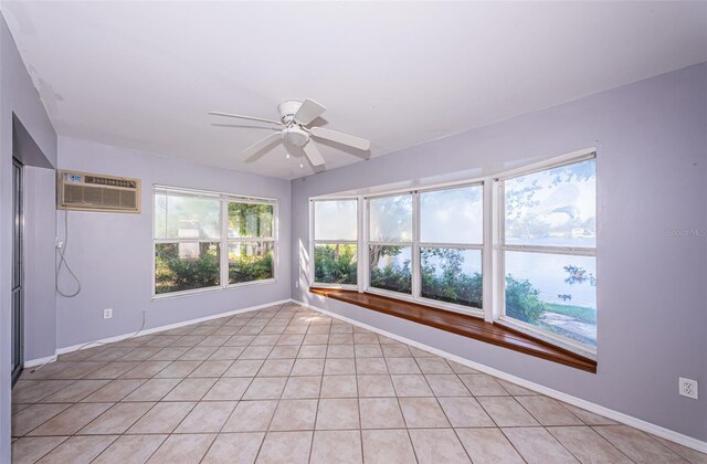 empty room featuring light tile patterned floors, baseboards, ceiling fan, and a wall mounted air conditioner