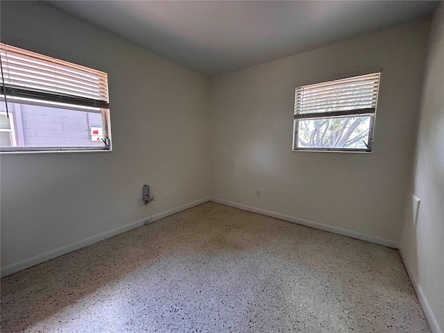 spare room featuring baseboards, speckled floor, and a wealth of natural light