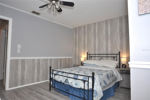 bedroom with a textured ceiling, wood-type flooring, ornamental molding, and ceiling fan