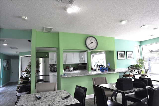 kitchen featuring light stone countertops, a wealth of natural light, white cabinets, and a kitchen bar