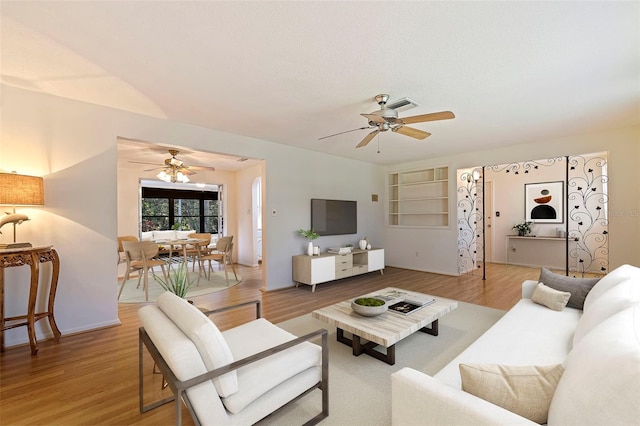 living room featuring ceiling fan, light hardwood / wood-style flooring, and built in shelves