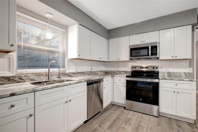 kitchen featuring sink, light wood-type flooring, appliances with stainless steel finishes, decorative light fixtures, and white cabinetry