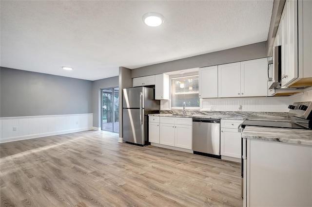 kitchen with light stone countertops, a textured ceiling, stainless steel appliances, light hardwood / wood-style flooring, and white cabinetry