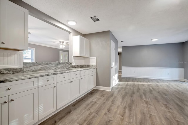 kitchen featuring white cabinets, ceiling fan, light wood-type flooring, and light stone countertops