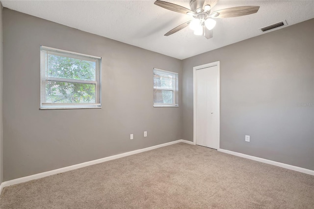 empty room with ceiling fan, a healthy amount of sunlight, carpet floors, and a textured ceiling