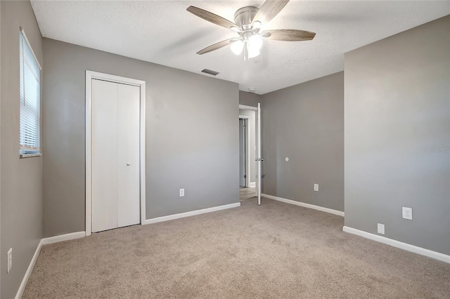 unfurnished bedroom with light carpet, a textured ceiling, a closet, and ceiling fan