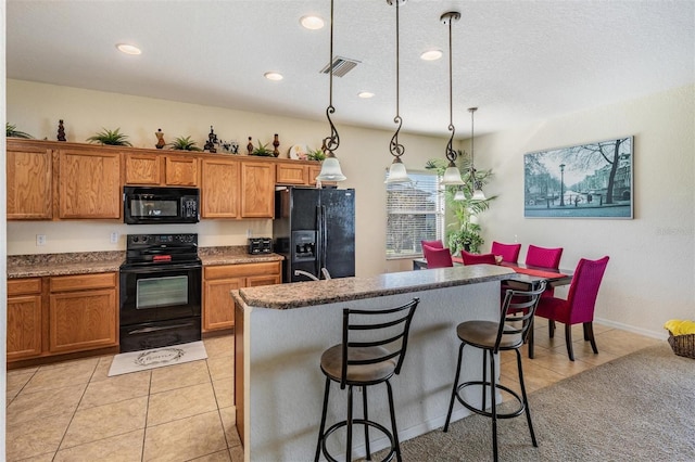 kitchen featuring hanging light fixtures, light tile patterned floors, a kitchen island, a breakfast bar, and black appliances