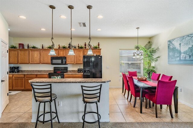 kitchen with hanging light fixtures, black appliances, a center island, a breakfast bar, and light tile patterned floors