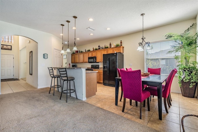 kitchen featuring light carpet, a kitchen island, a kitchen breakfast bar, black appliances, and decorative light fixtures