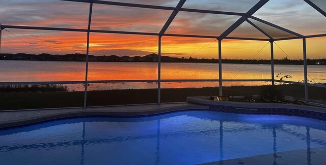 pool at dusk featuring a water view and a lanai