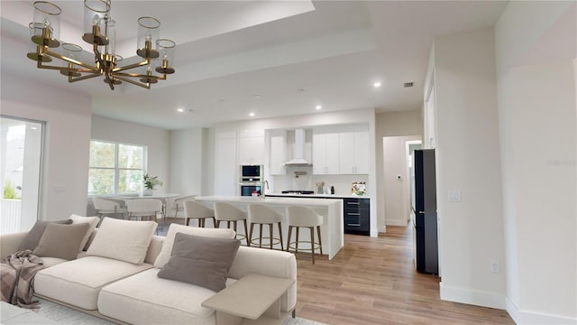 living room with light hardwood / wood-style floors, a notable chandelier, and a raised ceiling