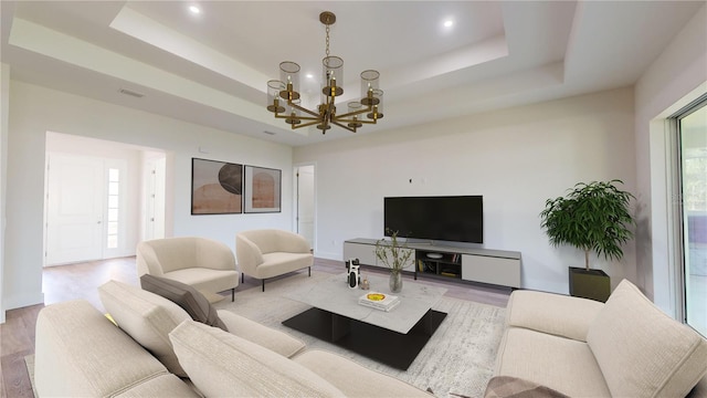 living room featuring a chandelier, light hardwood / wood-style flooring, and a tray ceiling