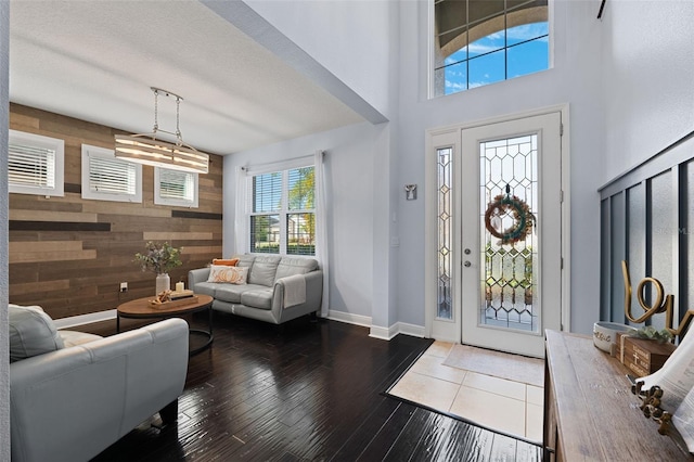 entryway with wooden walls, a textured ceiling, a towering ceiling, and dark hardwood / wood-style flooring