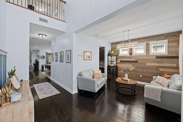 living room with a high ceiling, wooden walls, and dark hardwood / wood-style floors