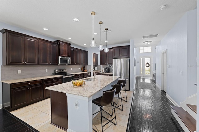 kitchen with light hardwood / wood-style floors, stainless steel appliances, decorative light fixtures, a breakfast bar area, and a center island with sink