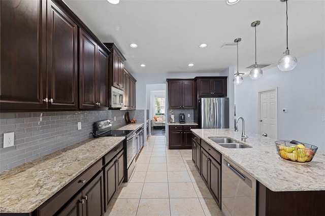 kitchen with dark brown cabinets, appliances with stainless steel finishes, a kitchen island with sink, pendant lighting, and sink