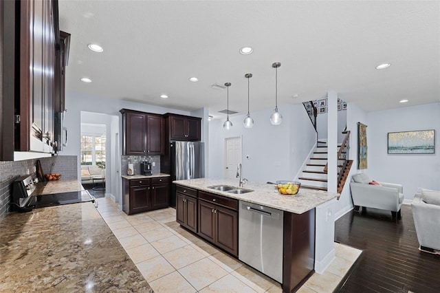 kitchen featuring a kitchen island with sink, hanging light fixtures, sink, appliances with stainless steel finishes, and light hardwood / wood-style floors