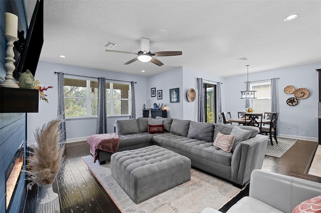 living room with a textured ceiling, wood-type flooring, and ceiling fan with notable chandelier