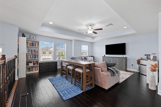 living room featuring a textured ceiling, ceiling fan, a tray ceiling, and dark hardwood / wood-style flooring