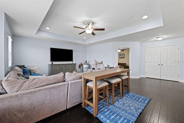 living room with ceiling fan, a tray ceiling, a textured ceiling, and dark hardwood / wood-style flooring