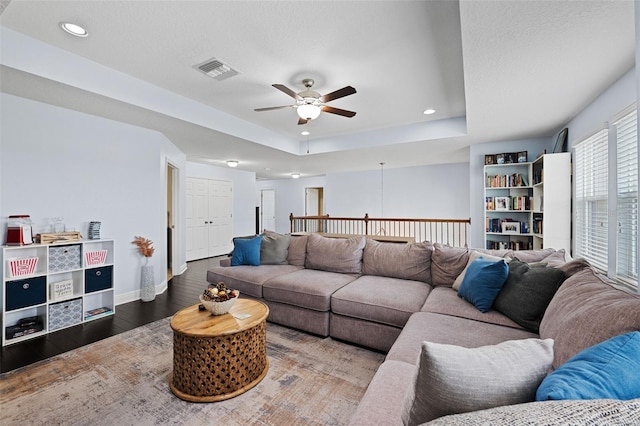 living room with ceiling fan, a raised ceiling, and wood-type flooring