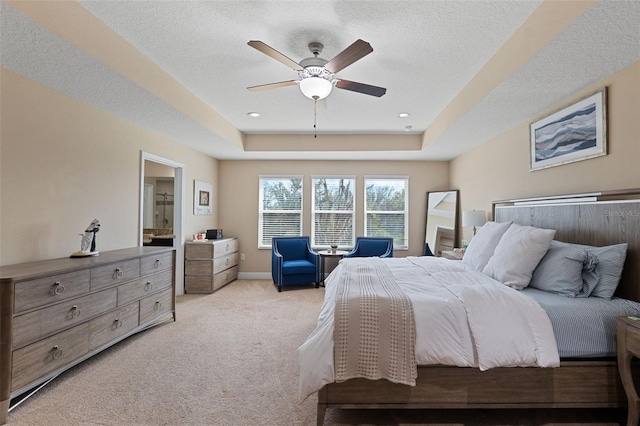 bedroom featuring a textured ceiling, light colored carpet, a tray ceiling, and ceiling fan