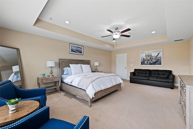 bedroom with light colored carpet, a raised ceiling, and ceiling fan