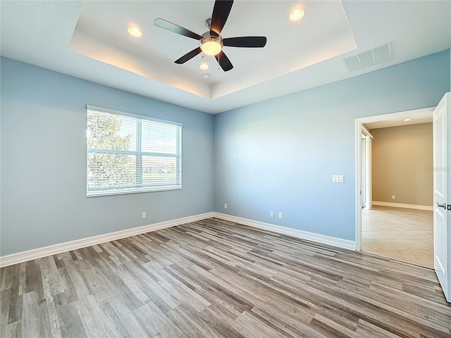 empty room with a raised ceiling, ceiling fan, and light hardwood / wood-style floors