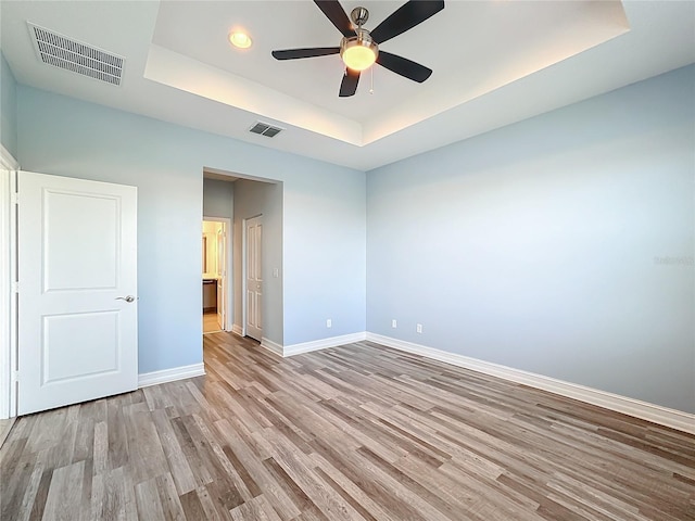 unfurnished bedroom featuring a tray ceiling, ceiling fan, and light hardwood / wood-style floors