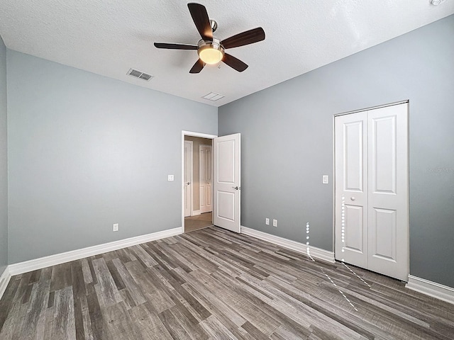 unfurnished bedroom with a textured ceiling, dark hardwood / wood-style flooring, a closet, and ceiling fan