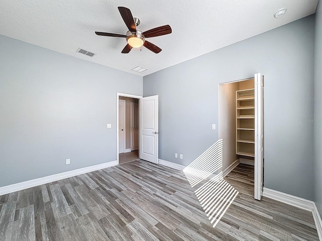 unfurnished bedroom featuring a textured ceiling, ceiling fan, hardwood / wood-style flooring, a spacious closet, and a closet