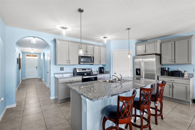 kitchen with stainless steel appliances, sink, a breakfast bar area, an island with sink, and pendant lighting