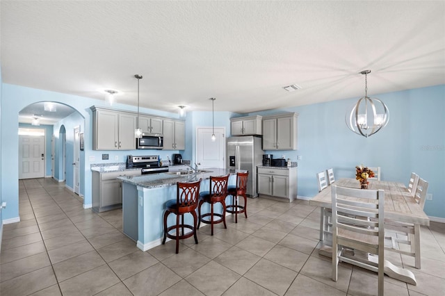 kitchen featuring appliances with stainless steel finishes, a kitchen breakfast bar, an inviting chandelier, a kitchen island with sink, and pendant lighting