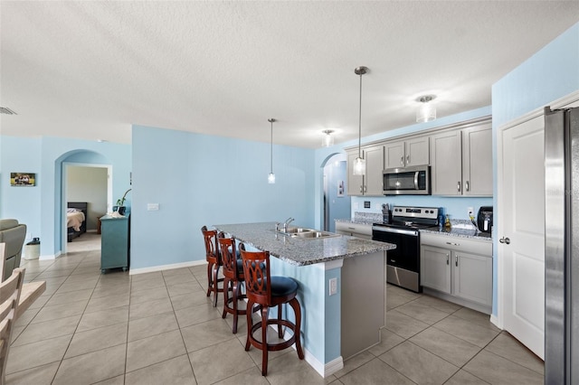 kitchen featuring stainless steel appliances, dark stone counters, a breakfast bar area, a kitchen island with sink, and pendant lighting