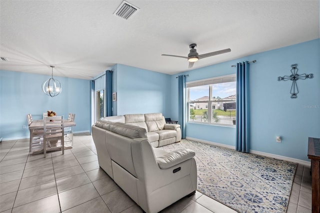 living room featuring ceiling fan with notable chandelier, a textured ceiling, and tile patterned floors