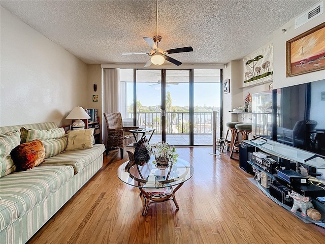 living room featuring ceiling fan, a textured ceiling, a wall of windows, and light hardwood / wood-style floors