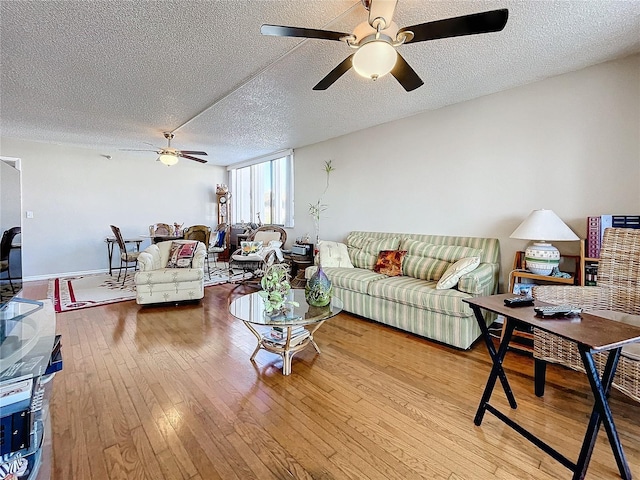 living room with ceiling fan, a textured ceiling, and light wood-type flooring