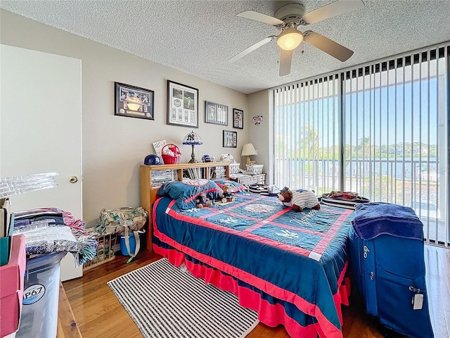 bedroom featuring wood-type flooring, access to exterior, ceiling fan, a water view, and a textured ceiling