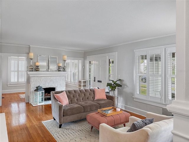 living area featuring a fireplace with flush hearth, baseboards, crown molding, and light wood finished floors