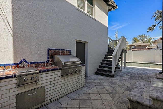 view of patio / terrace featuring a grill, fence, stairway, and exterior kitchen