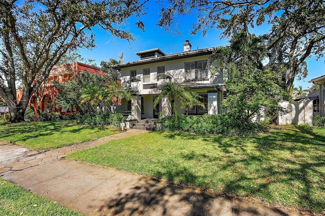 view of front facade featuring a balcony, a chimney, a front lawn, and stucco siding