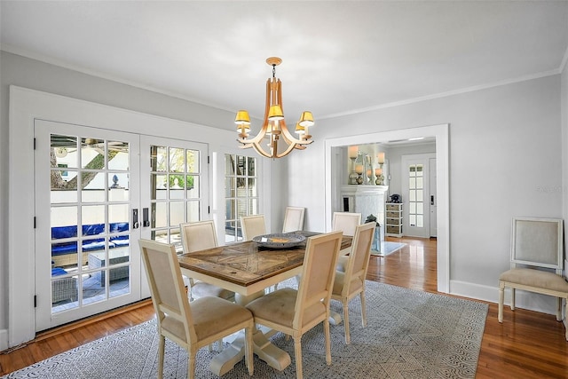 dining area with baseboards, wood finished floors, an inviting chandelier, crown molding, and french doors