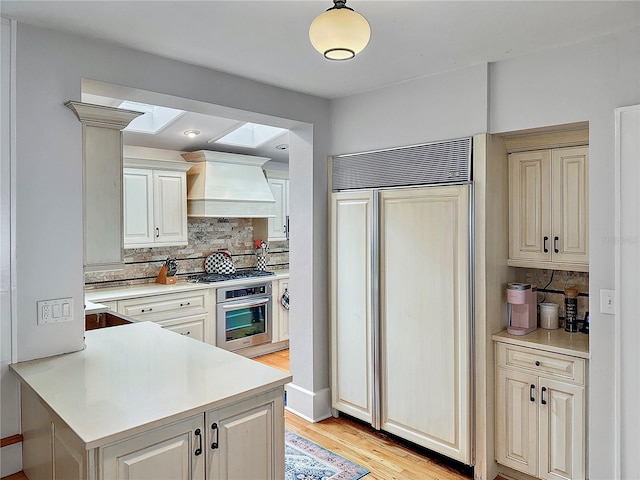 kitchen with a peninsula, light wood-style floors, light countertops, appliances with stainless steel finishes, and custom range hood