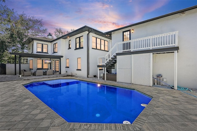 pool at dusk with an outdoor pool, a patio area, stairs, and an outdoor living space