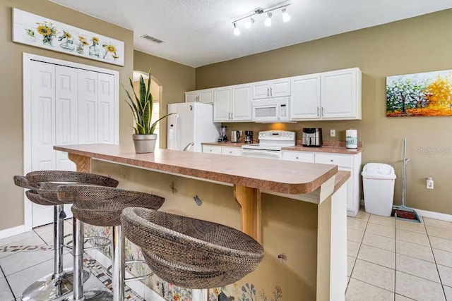 kitchen with a kitchen island, a breakfast bar, light tile patterned floors, white cabinets, and white appliances