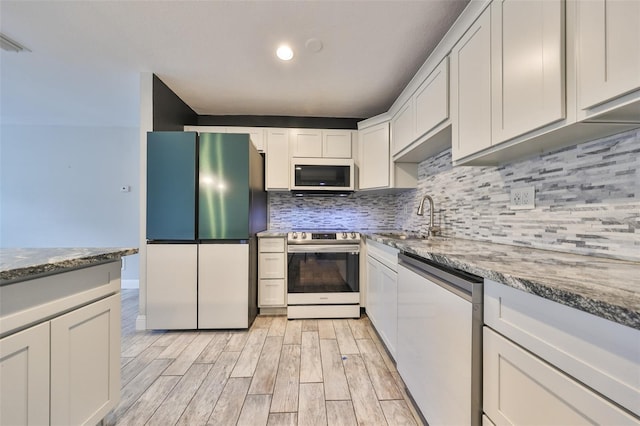 kitchen with appliances with stainless steel finishes, tasteful backsplash, light wood-type flooring, a sink, and dark stone countertops