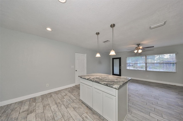 kitchen with white cabinetry, light stone counters, decorative light fixtures, and light wood-type flooring