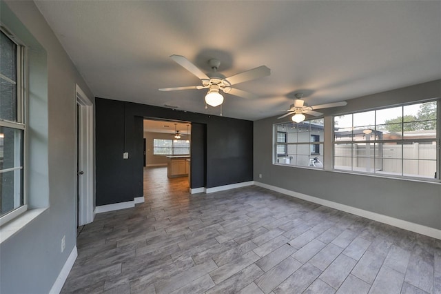 empty room with baseboards, ceiling fan, wood finished floors, and a wealth of natural light