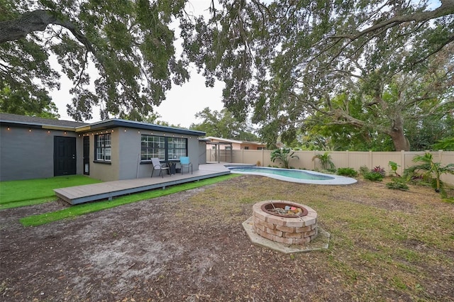 rear view of property with a swimming pool side deck, a fire pit, and a lawn